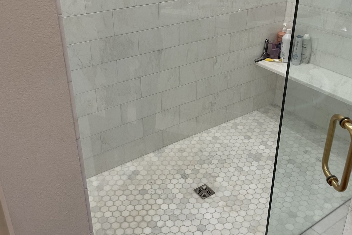 Walk-in shower with marble-look subway tile and a corner bench