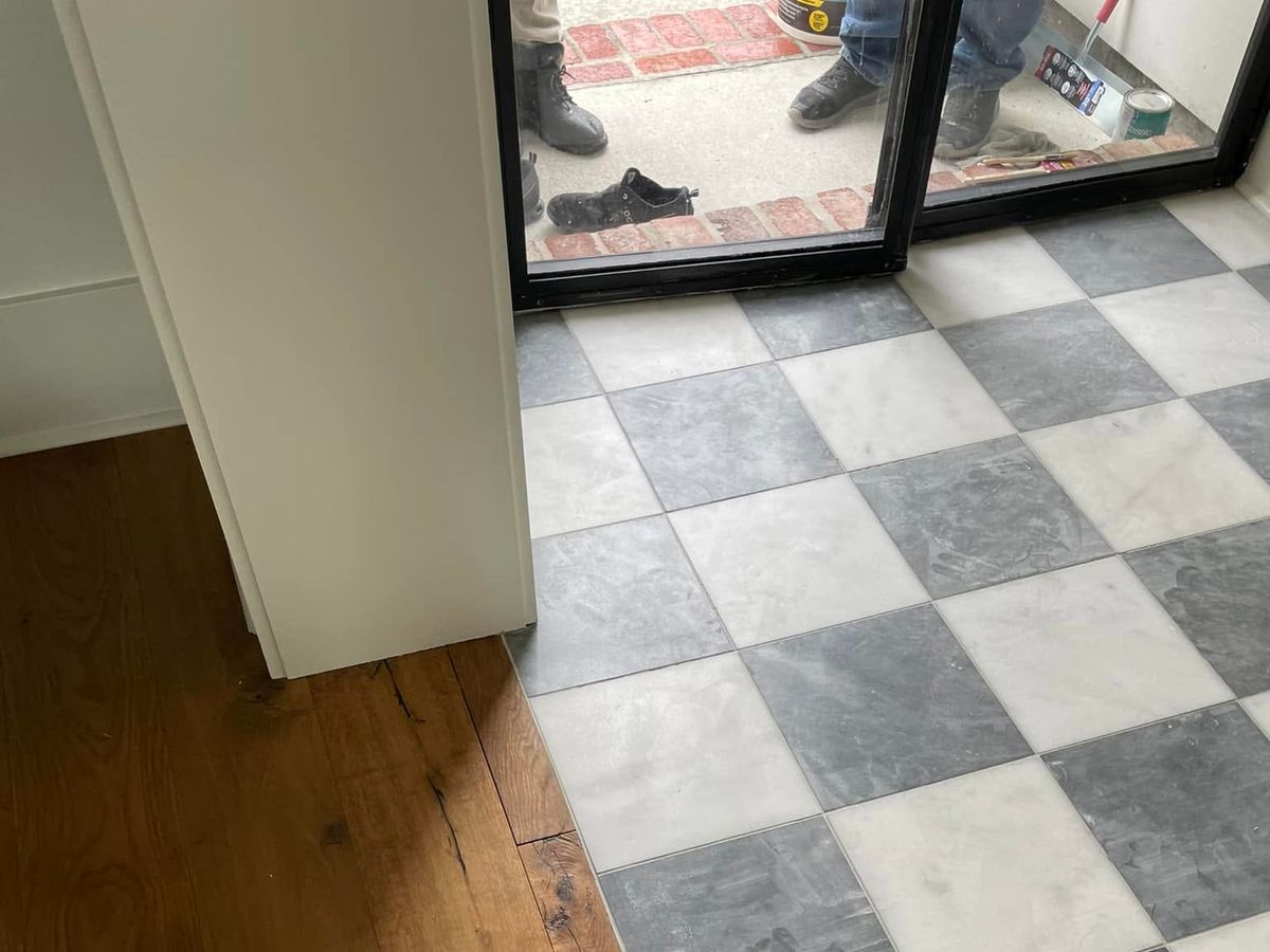 Wide-plank oak floor meeting marble checkerboard tile at a doorway
