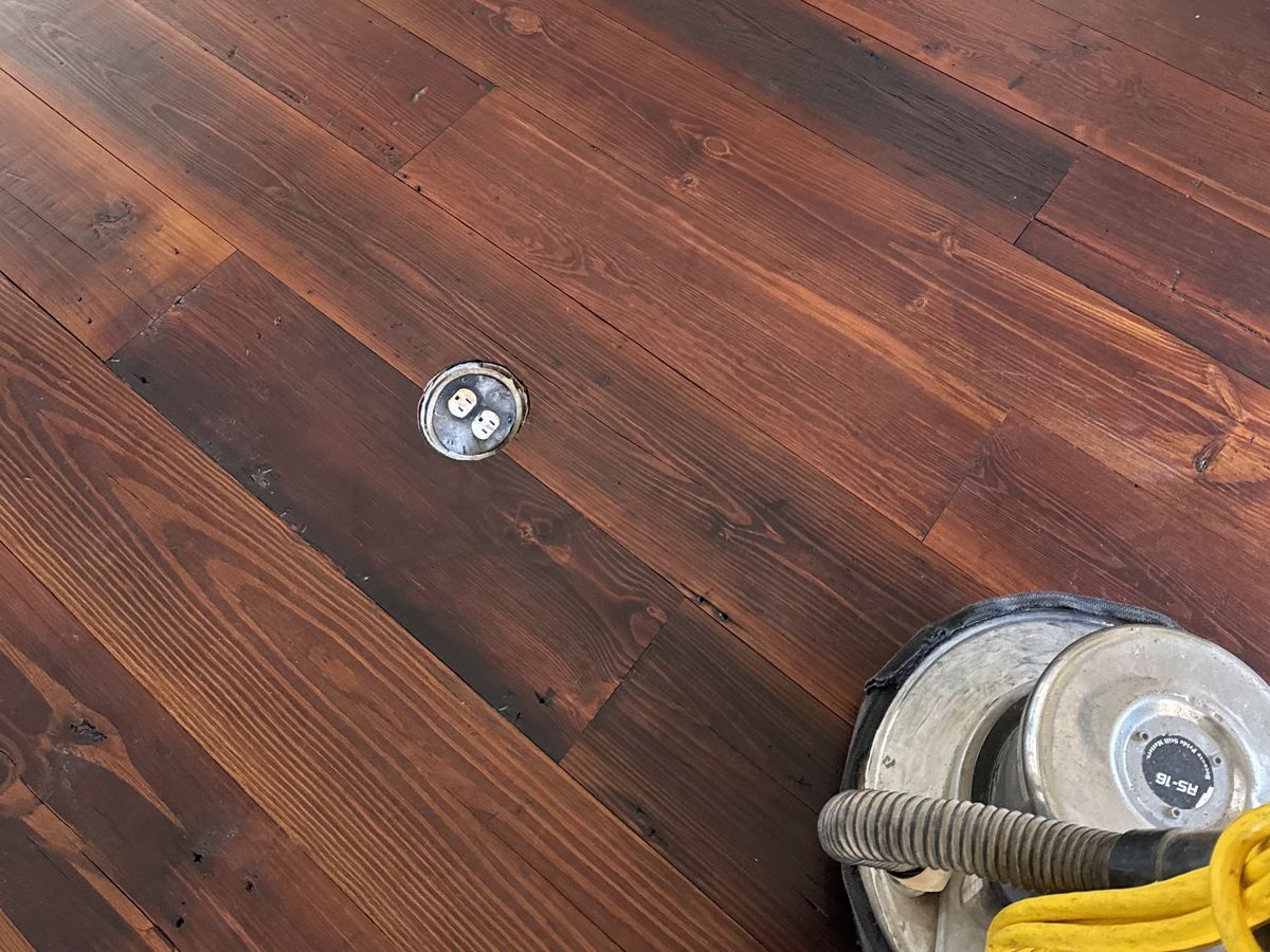 Floor buffer on a dark red-brown pine floor by a fireplace