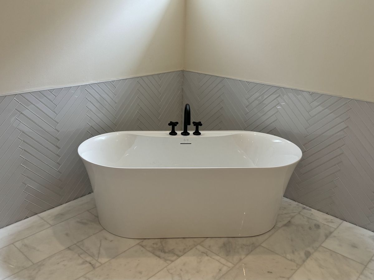 A white tub beside light gray herringbone wall tile
