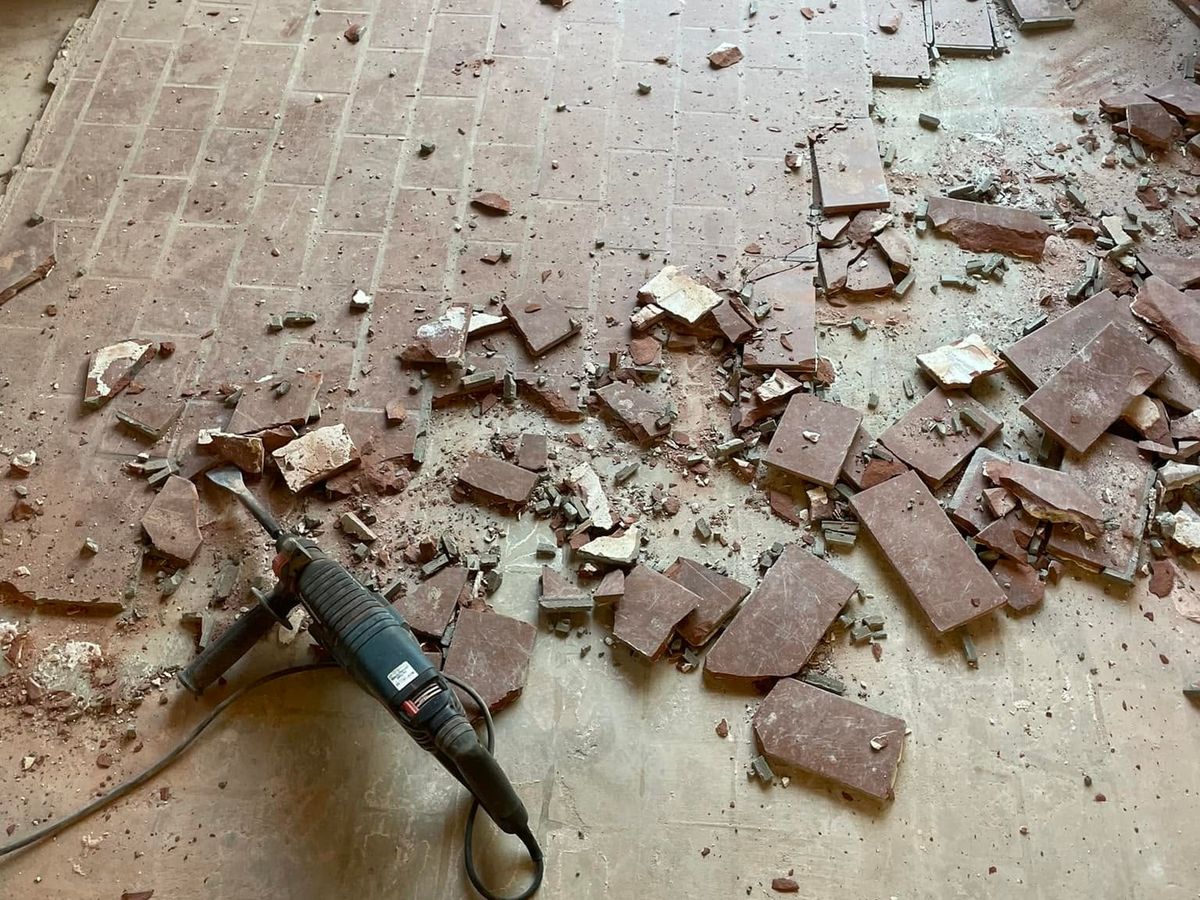 Old red brick-pattern floor tile being broken up with a hammer