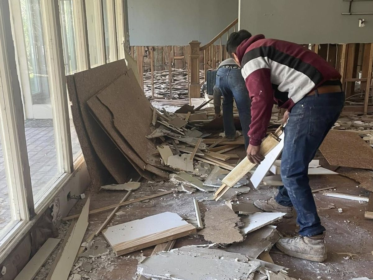 Two workers tearing out old walls and flooring inside a house