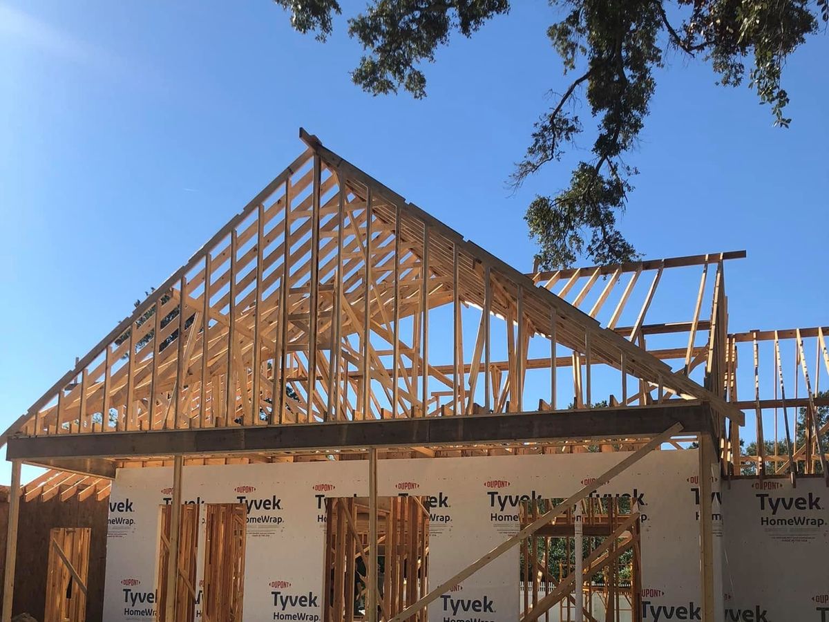 Home under construction with exposed trusses against a blue sky