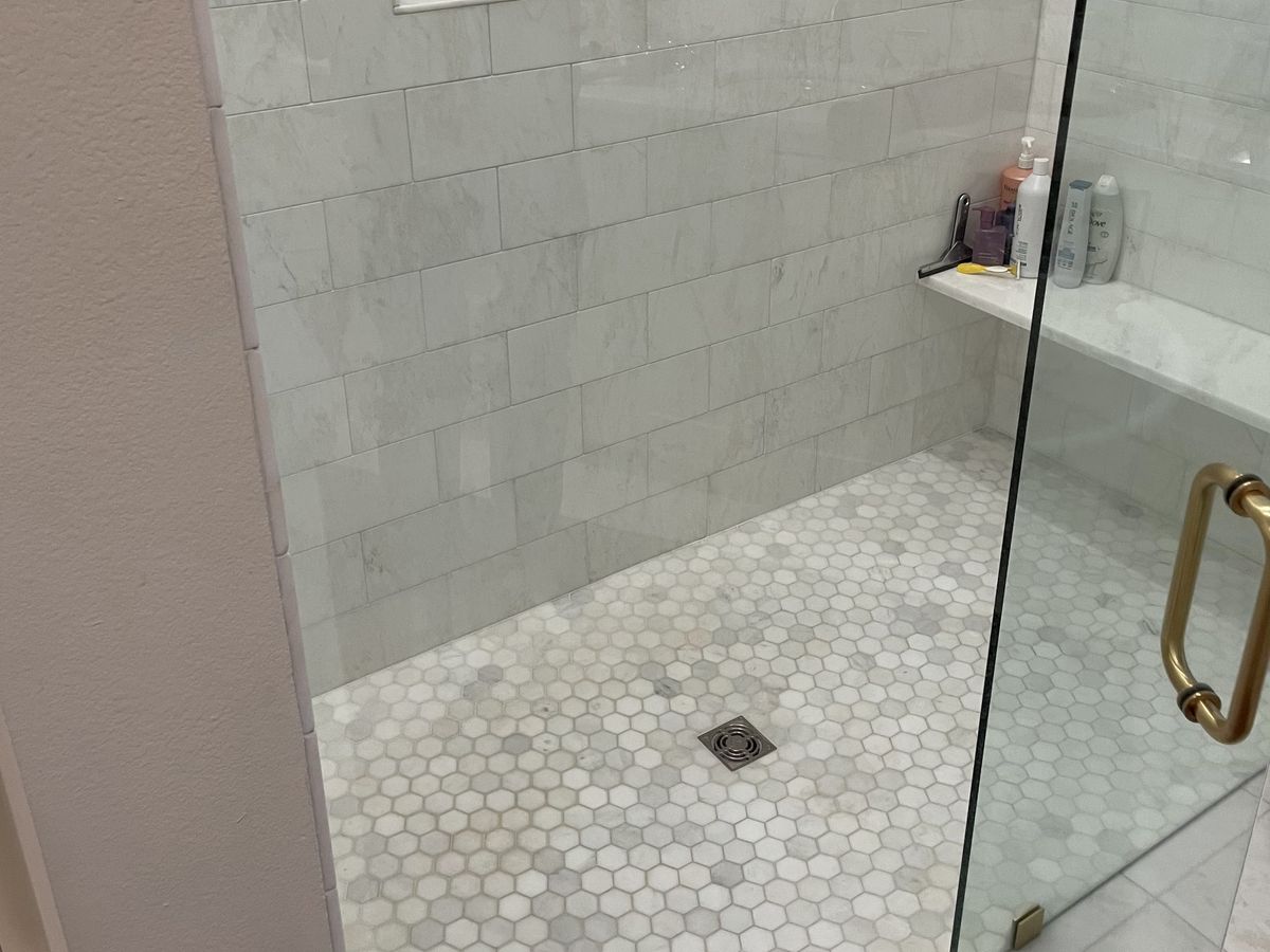 Shower behind a frameless glass door with a brass handle