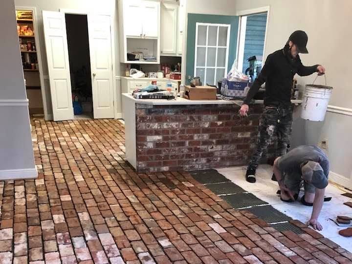 Workers setting old red brick floor beside a white kitchen island