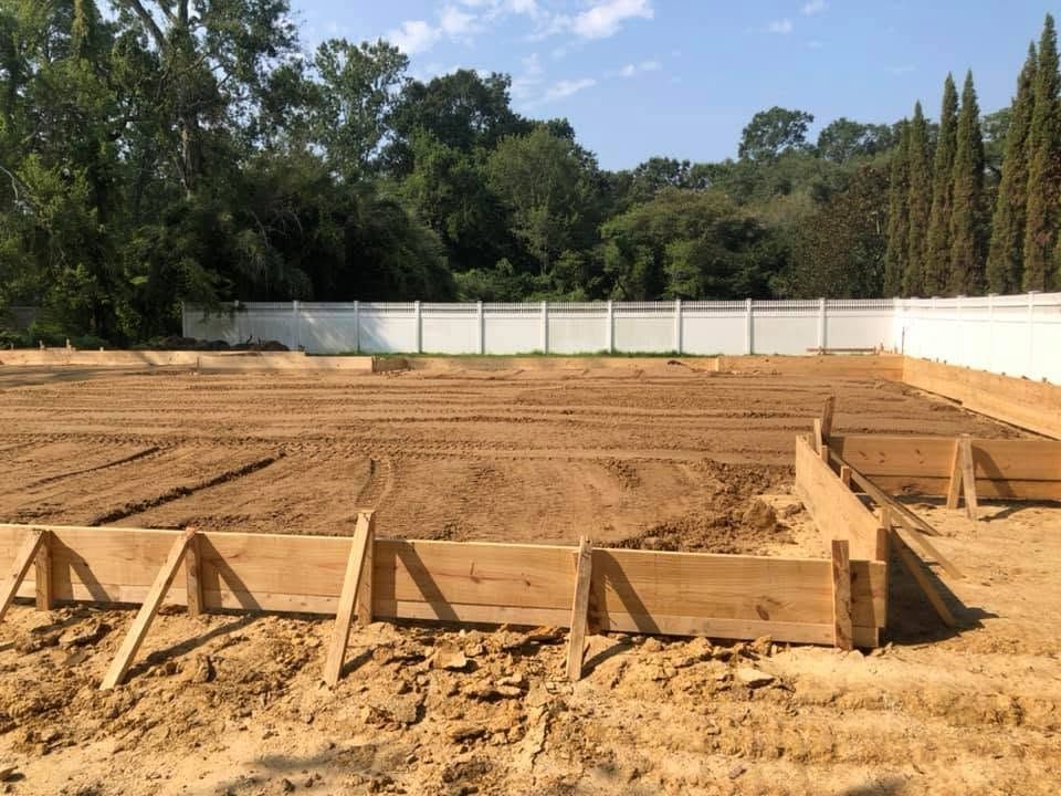 Staked slab forms around a graded pad ringed by cypress and oak trees