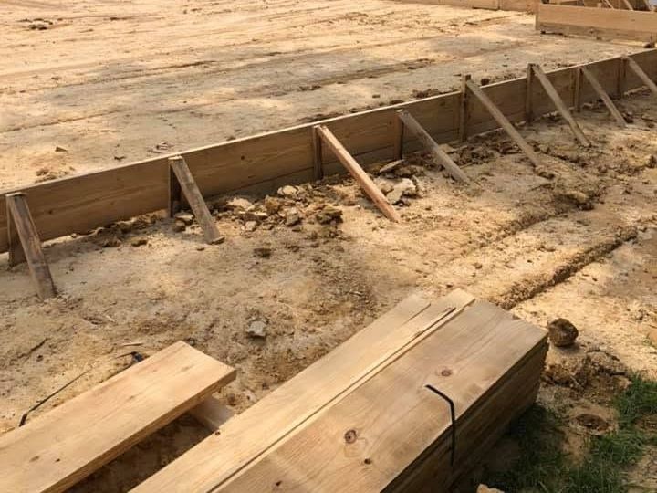 Packed tan house pad framed by slab forms beside a vinyl fence