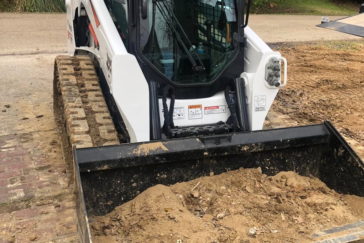 White track loader with a bucket of dirt on a graded lot