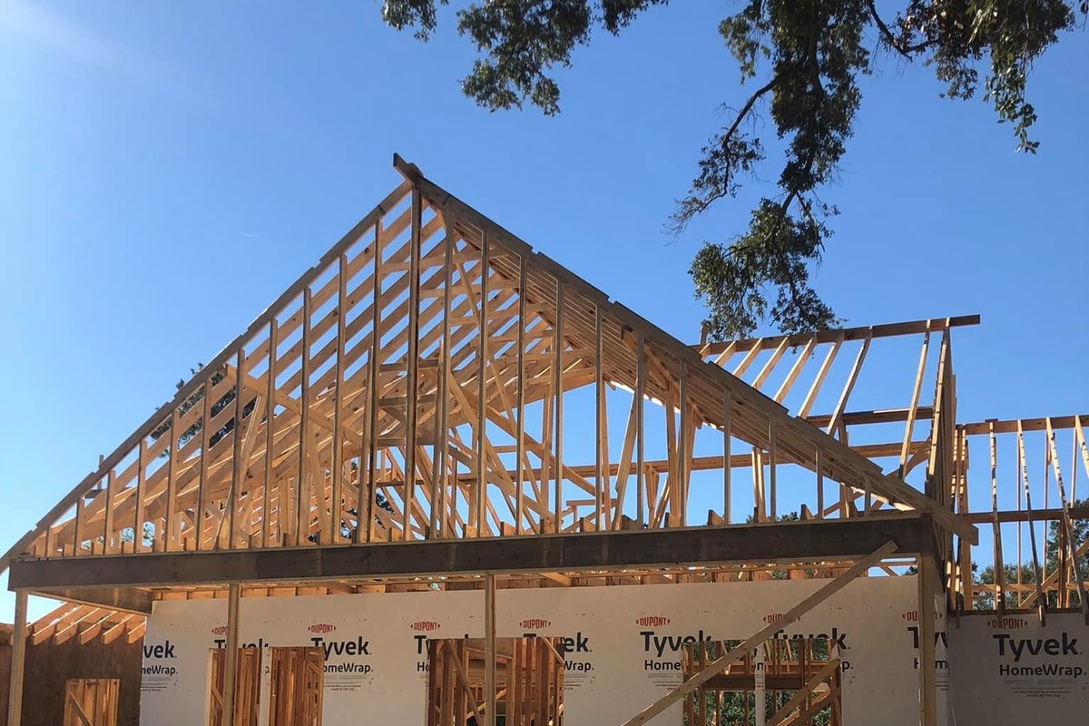 New house framing wrapped in white house wrap under a tall gable