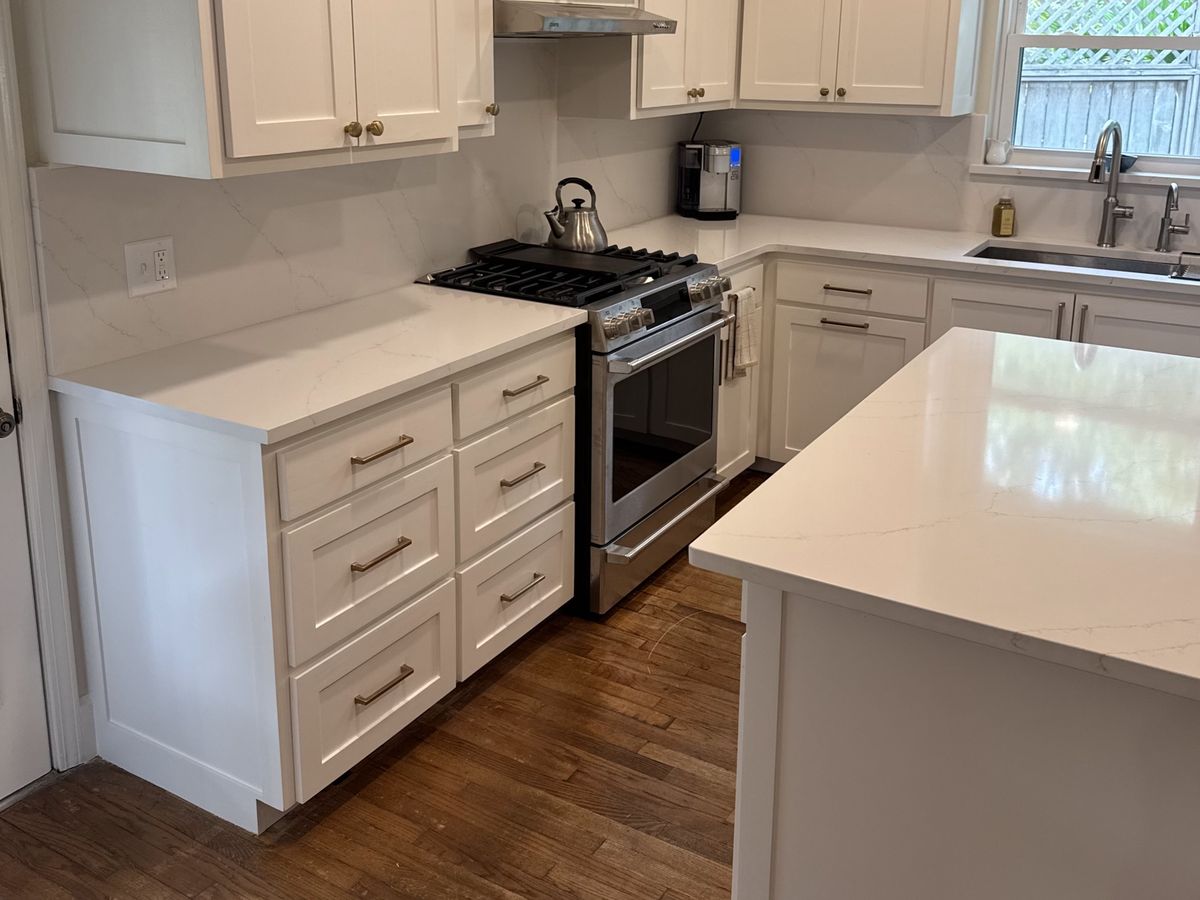 White kitchen with brass pulls and a quartz slab backsplash
