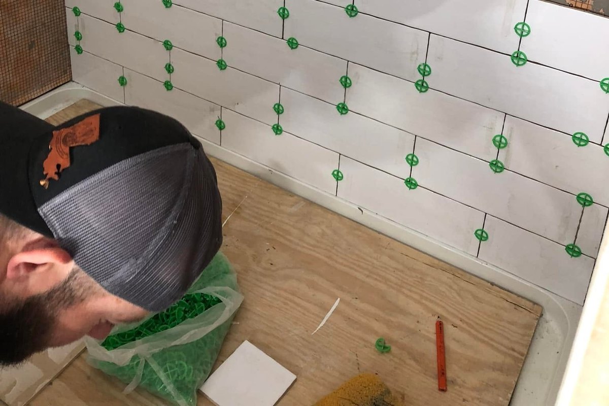 Shower being tiled in white rectangular tile in a brick pattern