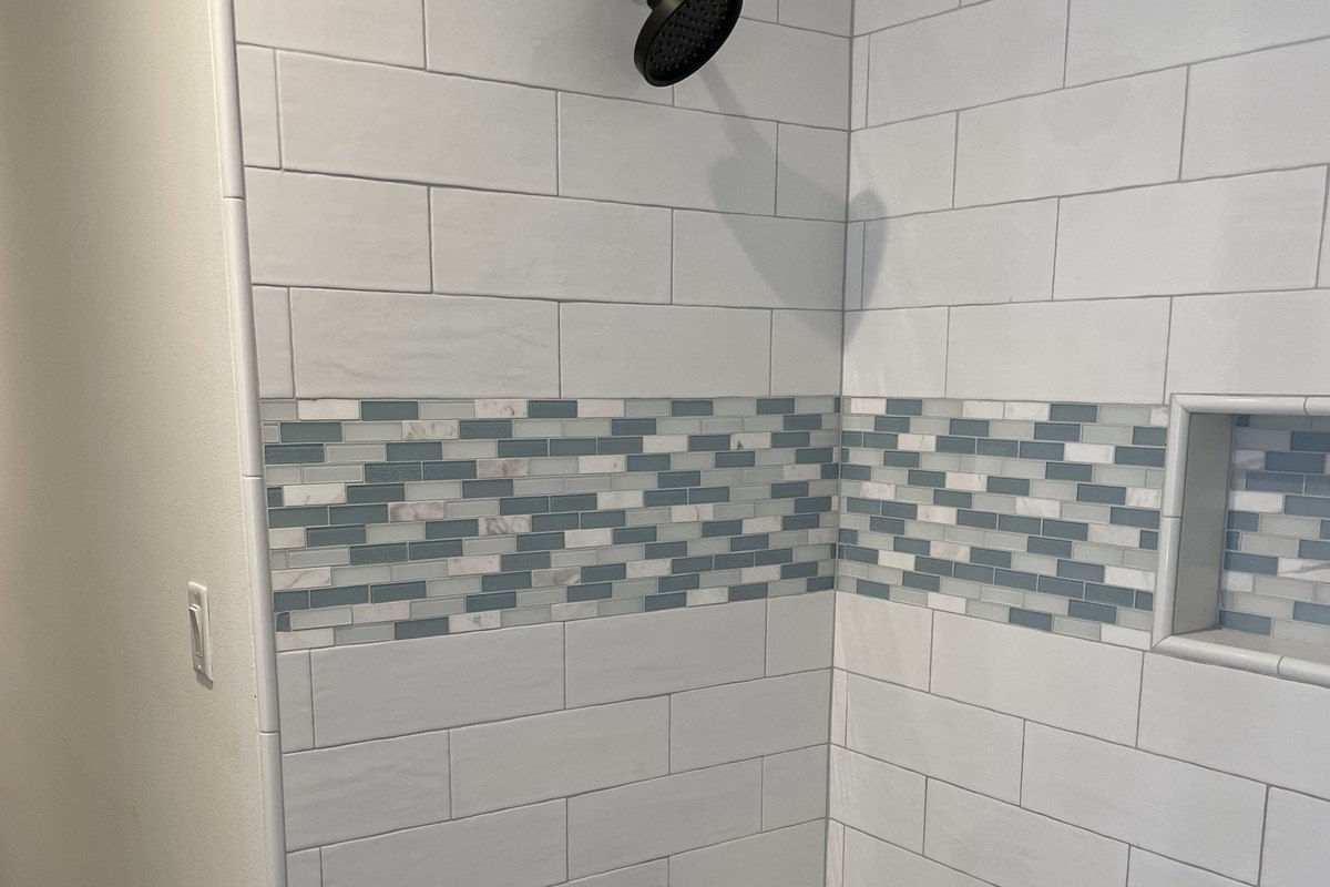 Shower wall in white subway tile with a glass mosaic band and niche