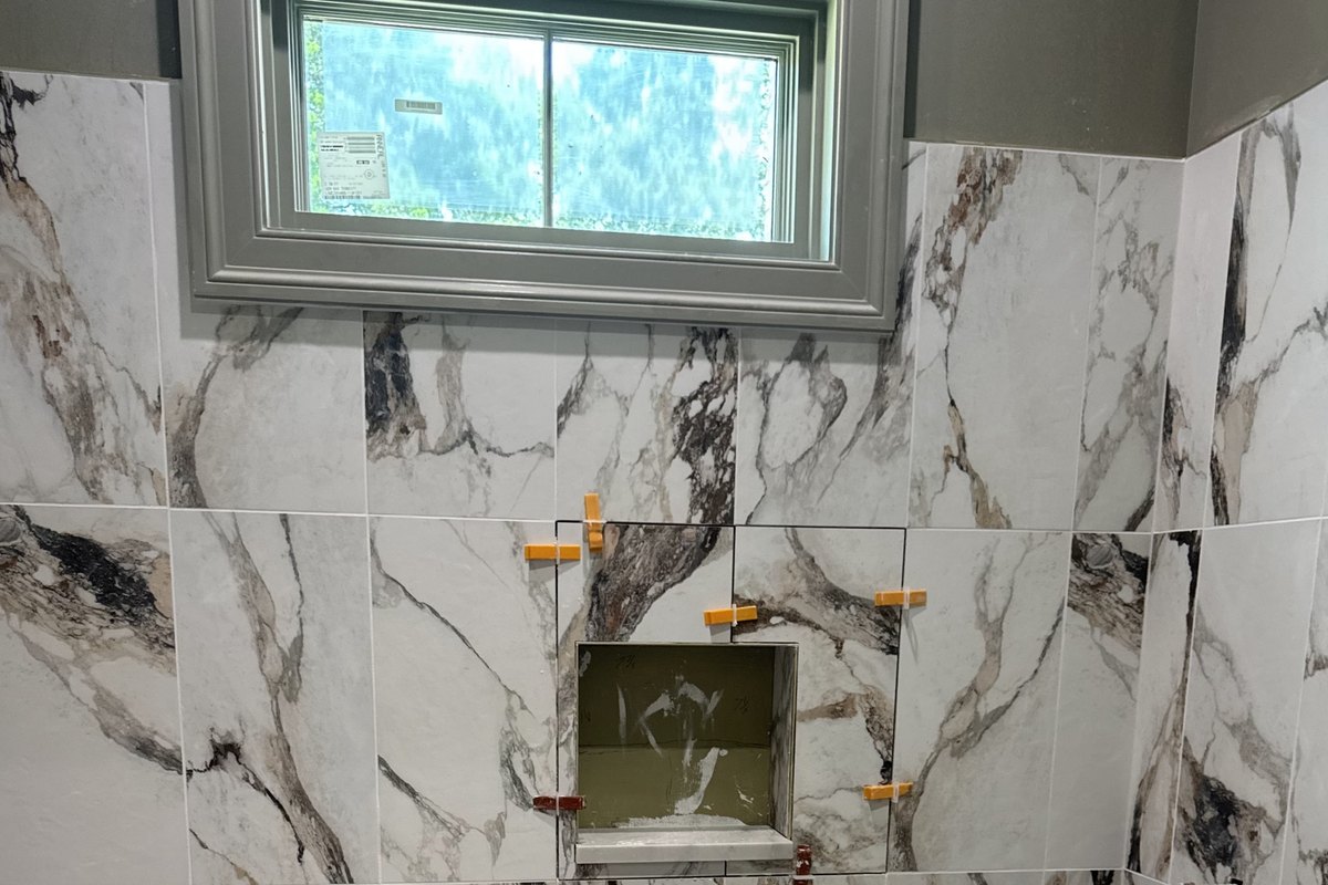 Large white porcelain shower tile with bold veining being set