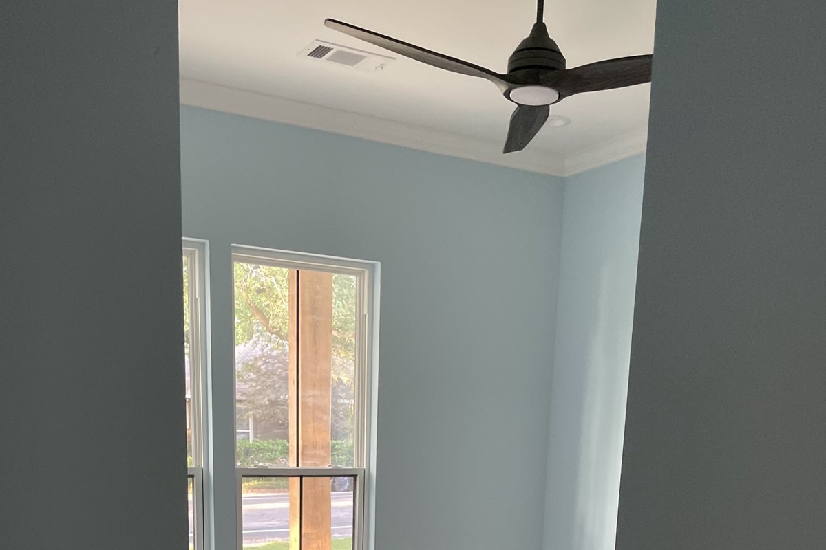 Pale blue bedroom with a black ceiling fan and a tall window