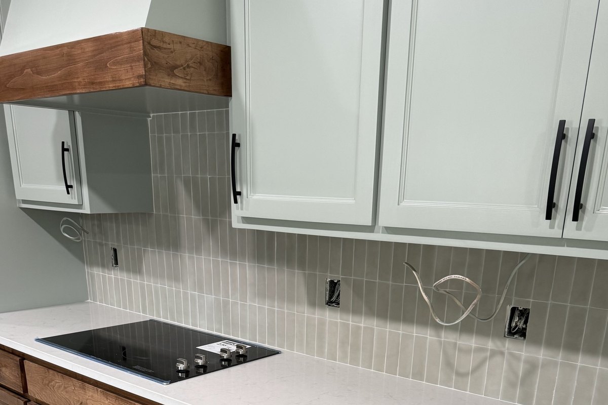 Sage upper cabinets over a gray stacked-tile backsplash