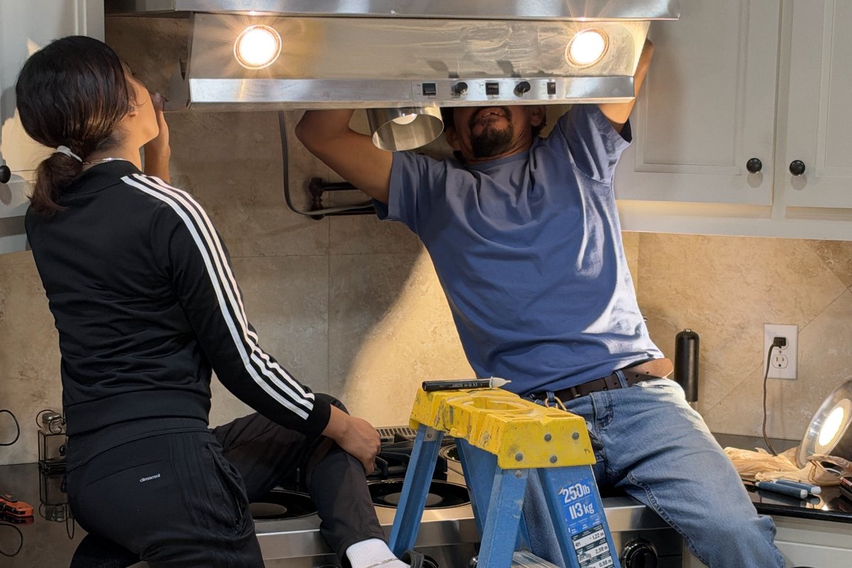 Stainless range hood being fitted over a gas range