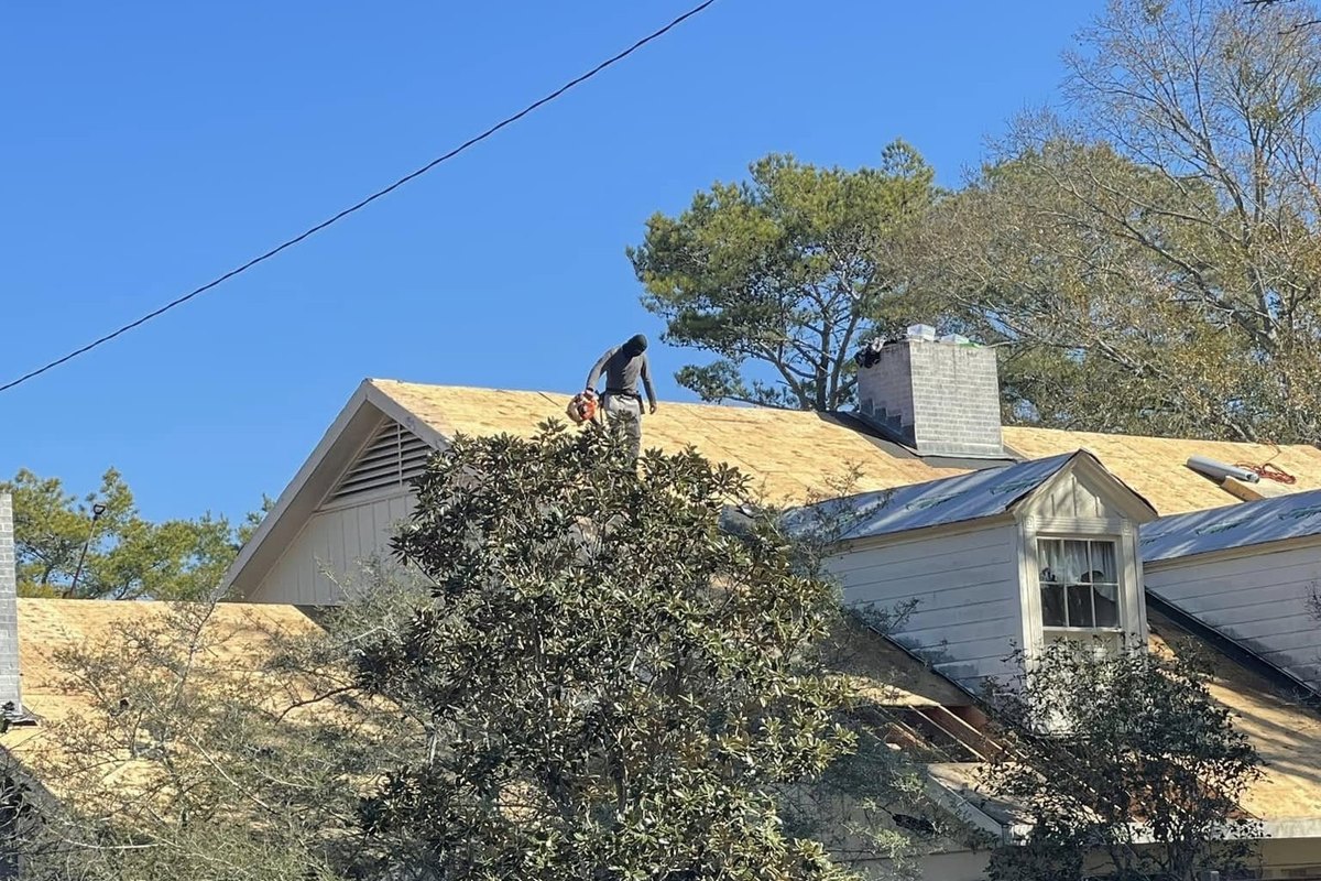Roofer on fresh plywood decking beside a gray metal roof section