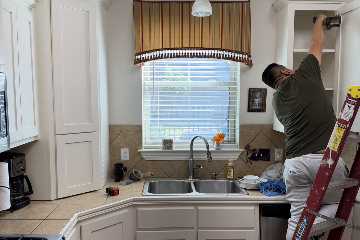 Kitchen cabinet trim being fitted by a worker on a ladder