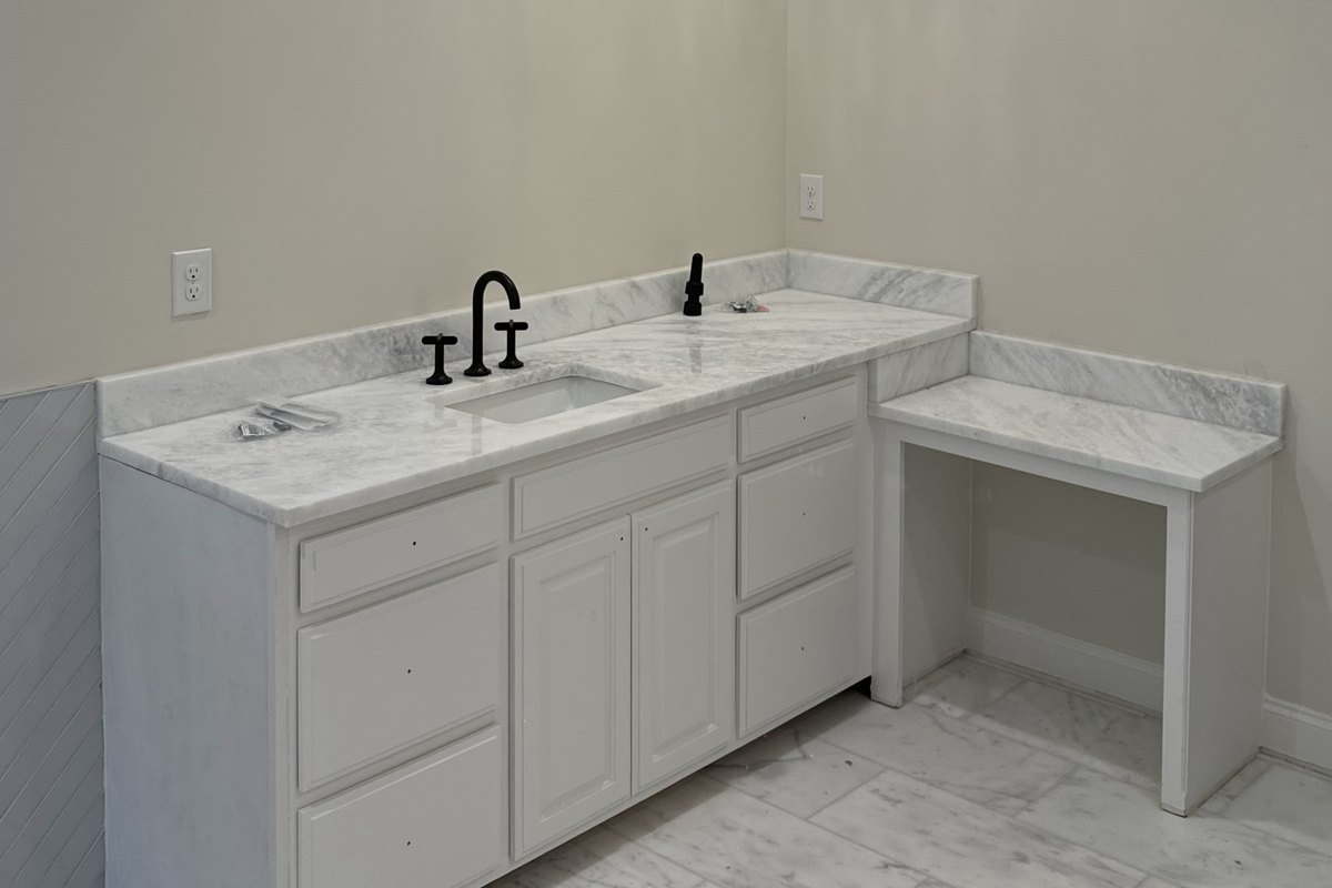 White vanity with a marble top and black faucets