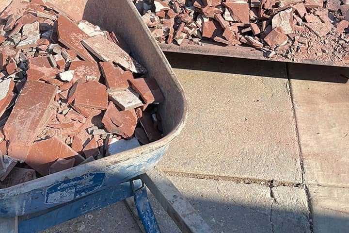 Broken old red floor tile piled in a wheelbarrow and loader bucket