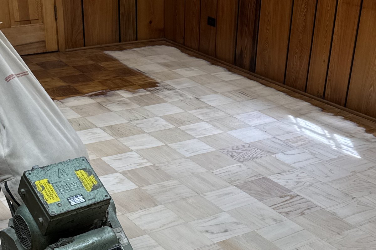 Old parquet wood floor mid-refinish under a drum sander