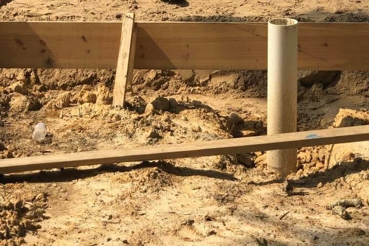 White PVC plumbing stubs rising from trenched dirt before the slab pour