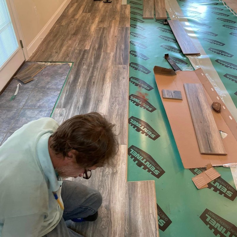 Installer laying gray wood-look plank flooring on green underlayment