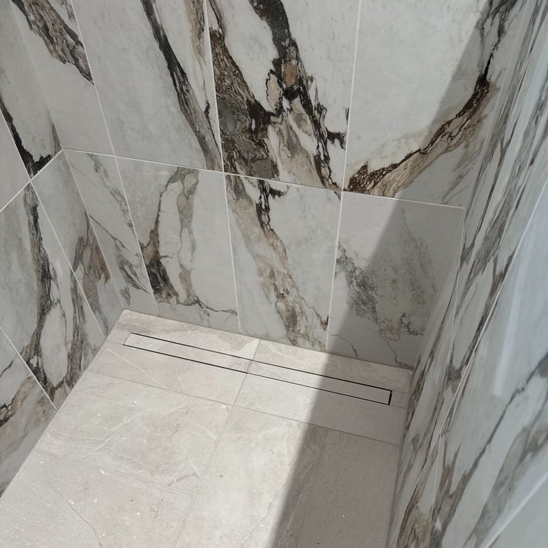Dark-veined white shower tile over a light stone-look floor