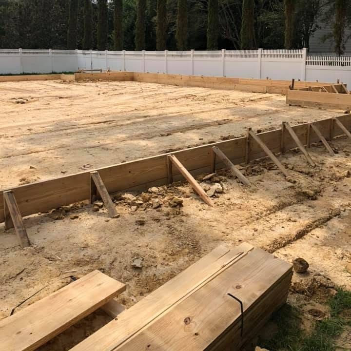 Graded house pad of packed fill inside staked wood form boards